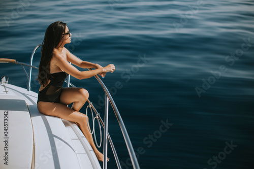 Young woman in swimwear and sunglasses sitting on a yacht deck