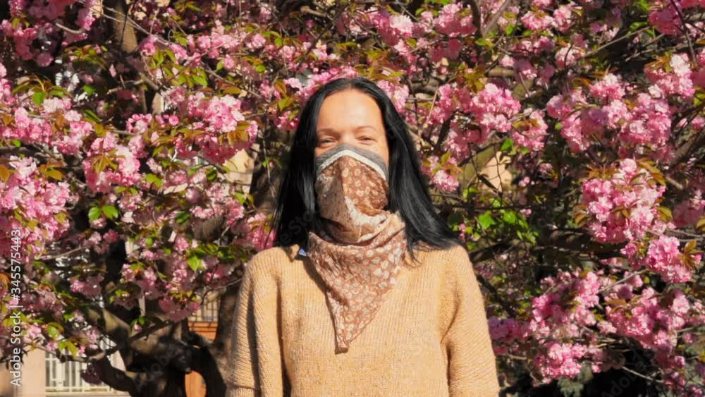 portrait caucasian woman in pollution face guard posing in park looking camera smiling on the background pink cherry blossoms in sunlight slow motion portrait caucasian woman in pollution face guard posing in park looking camera smiling on the background pink cherry blossoms in sunlight slow motion