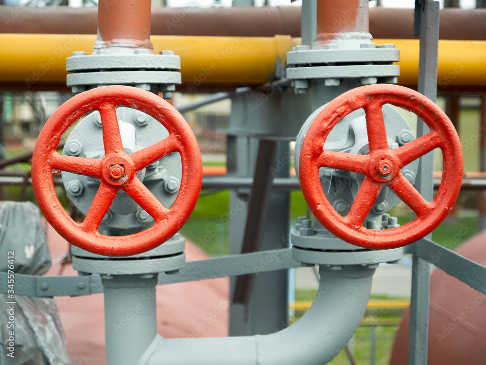 Two red valves with red steering wheels over background of pipes at chemical plant.