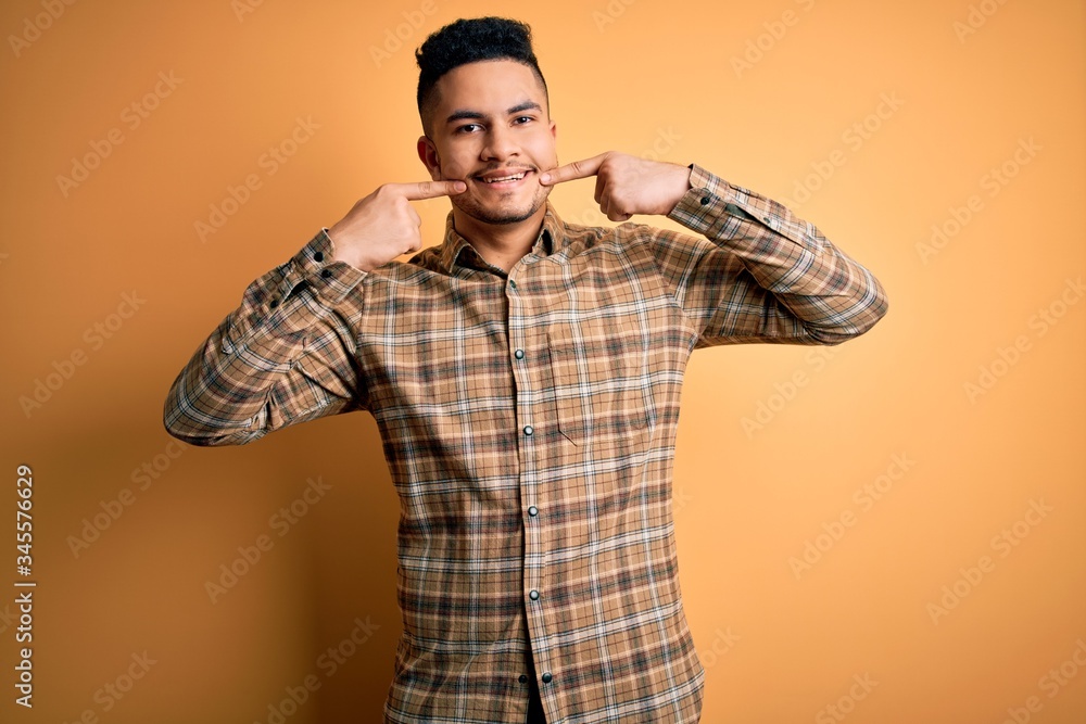 Young handsome man wearing casual shirt standing over isolated yellow background smiling cheerful showing and pointing with fingers teeth and mouth. Dental health concept. Young handsome man wearing casual shirt standing over isolated yellow background smiling cheerful showing and pointing with fingers teeth and mouth. Dental health concept.