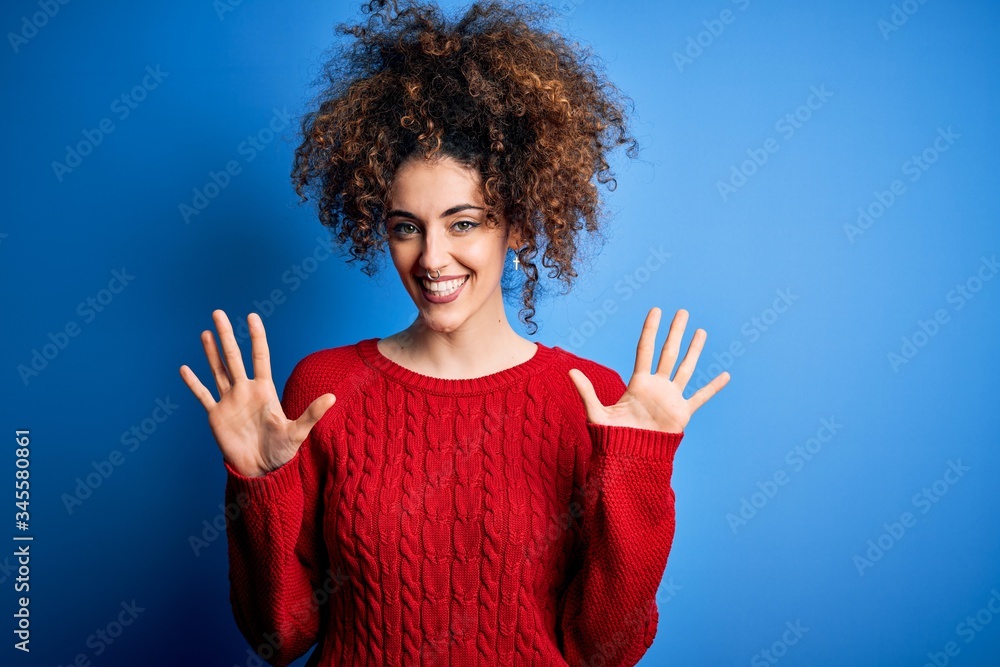 Young beautiful woman with curly hair and piercing wearing casual red sweater showing and pointing up with fingers number ten while smiling confident and happy. Young beautiful woman with curly hair and piercing wearing casual red sweater showing and pointing up with fingers number ten while smiling confident and happy.