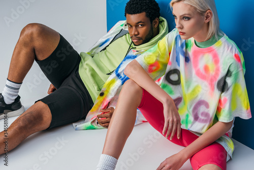 beautiful stylish interracial couple posing in colorful futuristic look on grey and blue