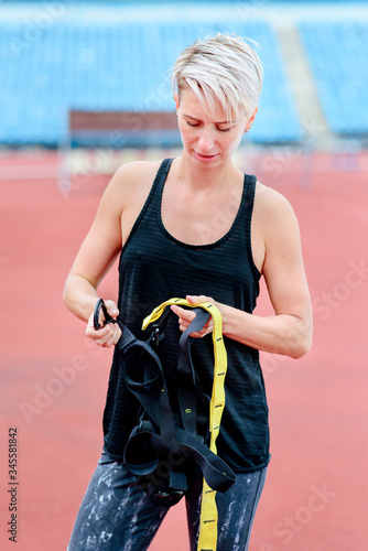 woman with short cut preparing for training with TRX outdoor , .checks fastener system, carabiner