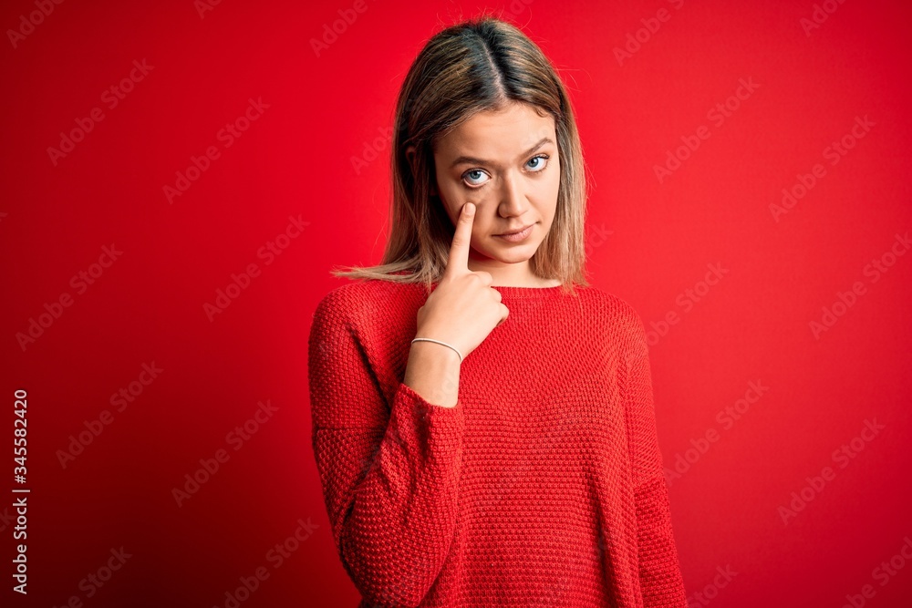 Young beautiful blonde woman wearing casual sweater over red isolated background Pointing to the eye watching you gesture, suspicious expression Young beautiful blonde woman wearing casual sweater over red isolated background Pointing to the eye watching you gesture, suspicious expression