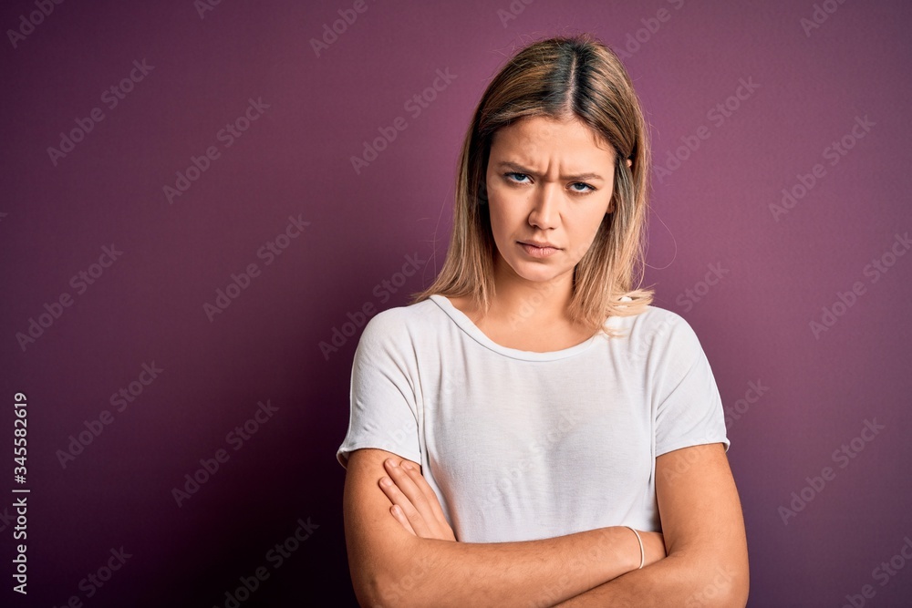 Fototapeta premium Young beautiful blonde woman wearing casual white t-shirt over purple isolated background skeptic and nervous, disapproving expression on face with crossed arms. Negative person.