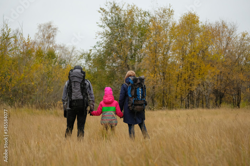 Mom, dad and daughter go camping. Family of tourists with backpacks on the background of autumn forest.