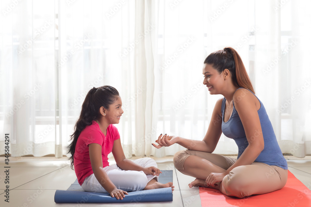 Mother and daughter sitting on exercise mat 
