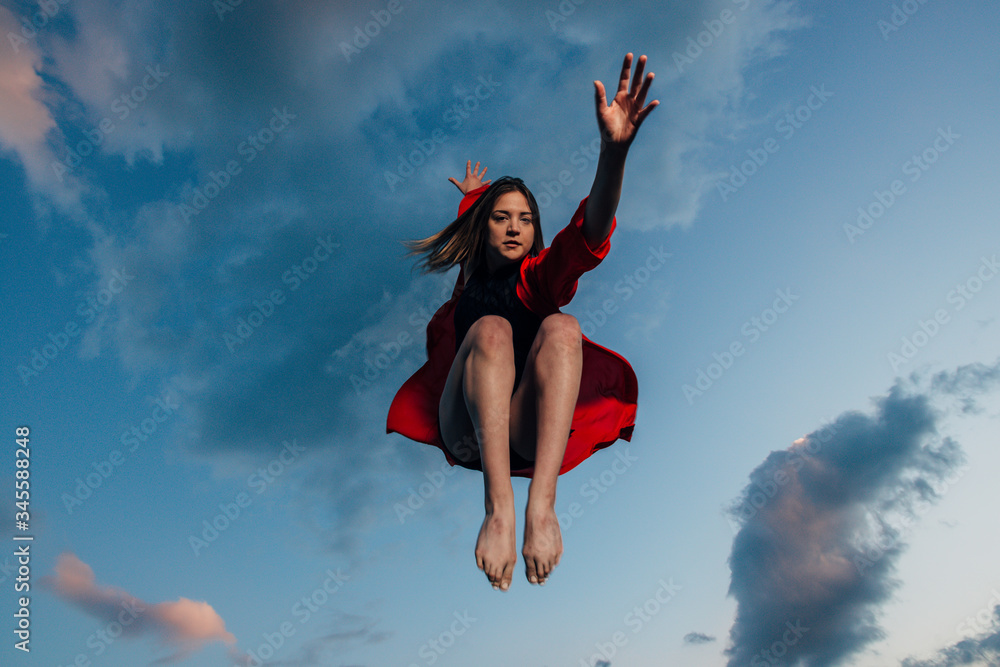 Playful woman jumping at blue cloudy sky