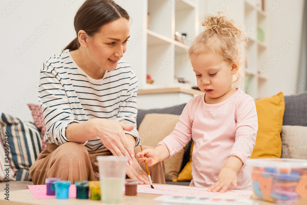 Young woman spending time with daughter at home teaching her to paint pictures, horizontal shot Young woman spending time with daughter at home teaching her to paint pictures, horizontal shot