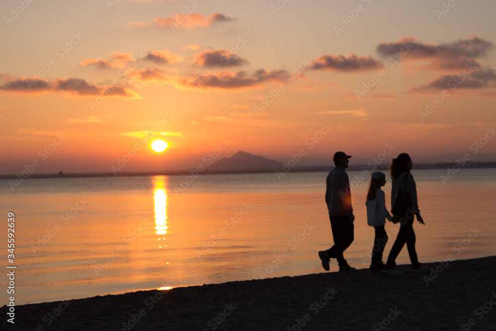 Three people walking in the beach at sunset moment

