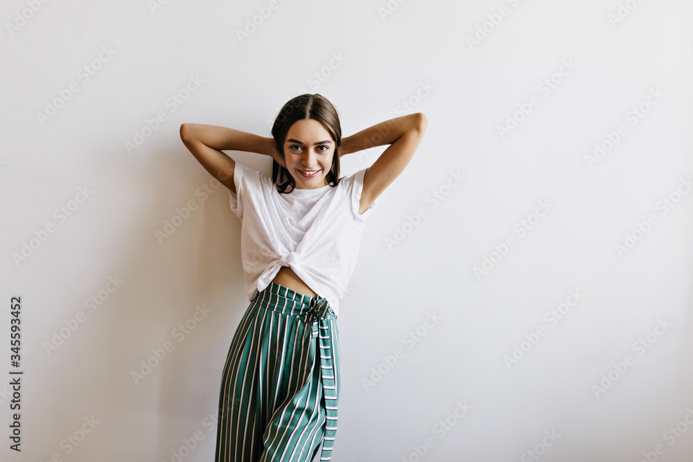 Joyful female model in pajama playing with her hair. Laughing young woman in green pants standing on white background. Joyful female model in pajama playing with her hair. Laughing young woman in green pants standing on white background.