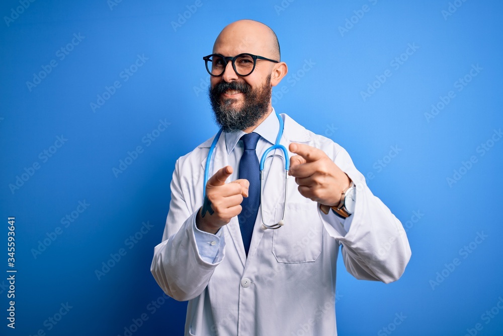 Handsome bald doctor man with beard wearing glasses and stethoscope over blue background pointing fingers to camera with happy and funny face. Good energy and vibes. Handsome bald doctor man with beard wearing glasses and stethoscope over blue background pointing fingers to camera with happy and funny face. Good energy and vibes.