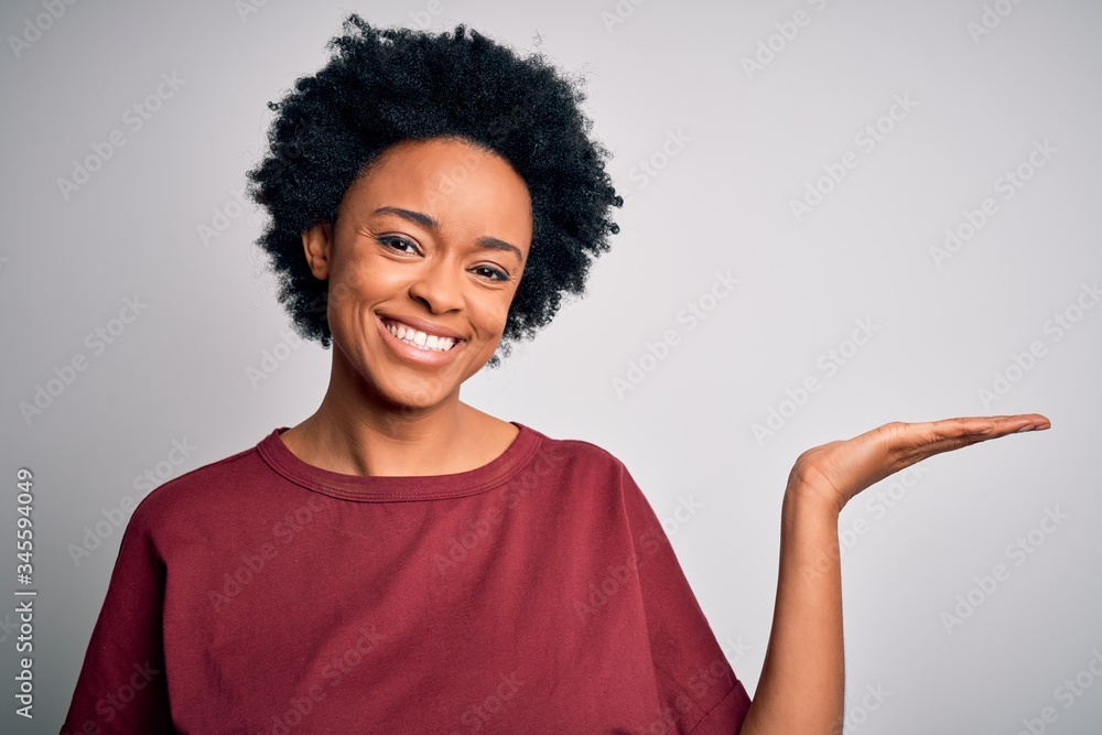 Young beautiful African American afro woman with curly hair wearing casual t-shirt standing smiling cheerful presenting and pointing with palm of hand looking at the camera. Young beautiful African American afro woman with curly hair wearing casual t-shirt standing smiling cheerful presenting and pointing with palm of hand looking at the camera.
