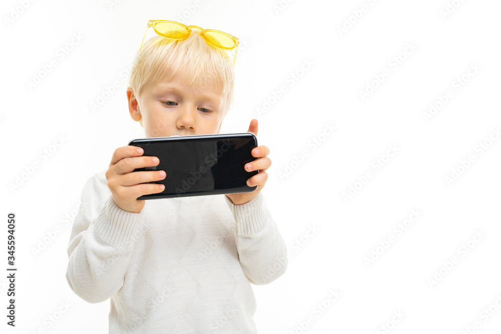 Little blonde caucasian boy play phone games isolated on white background Little blonde caucasian boy play phone games isolated on white background