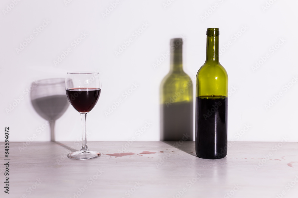 Bottle with wine and glass, red puddle of wine on the table. Cleaning after party concept. Bottle with wine and glass, red puddle of wine on the table. Cleaning after party concept.