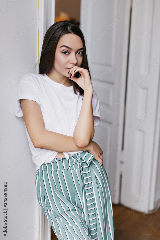 Slim interested girl in white t-shirt posing in her apartment. Indoor photo of fascinating woman relaxing at home. Slim interested girl in white t-shirt posing in her apartment. Indoor photo of fascinating woman relaxing at home.