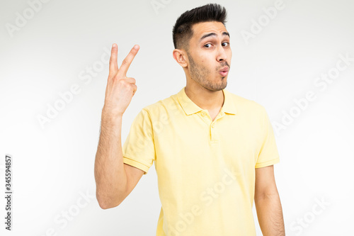 Caucasian man in a yellow T-shirt shows two fingers on a white isolated background © Ivan Traimak