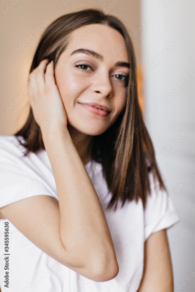 Gorgeous dark-haired young lady posing with interested smile. Indoor photo of amazing female model touching her hair on blur background. Gorgeous dark-haired young lady posing with interested smile. Indoor photo of amazing female model touching her hair on blur background.
