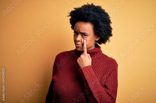 Young beautiful African American afro woman with curly hair wearing casual turtleneck sweater Pointing to the eye watching you gesture, suspicious expression © Krakenimages.com