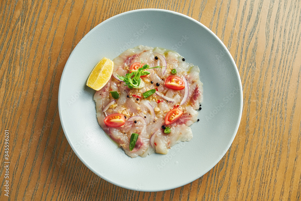 Chilled sea bass carpaccio with red onion, cherry tomatoes and hot chili peppers in a beige bowl on a wooden background. Close up, selective focus Chilled sea bass carpaccio with red onion, cherry tomatoes and hot chili peppers in a beige bowl on a wooden background. Close up, selective focus