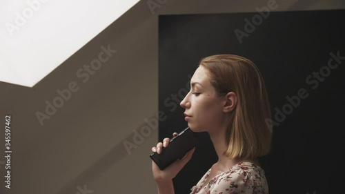 a young woman stands wistfully with her phone in her hand, slinking it into her chin photo