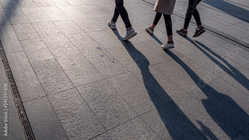 Legs of young women walking on the sidewalk and casting long shadows