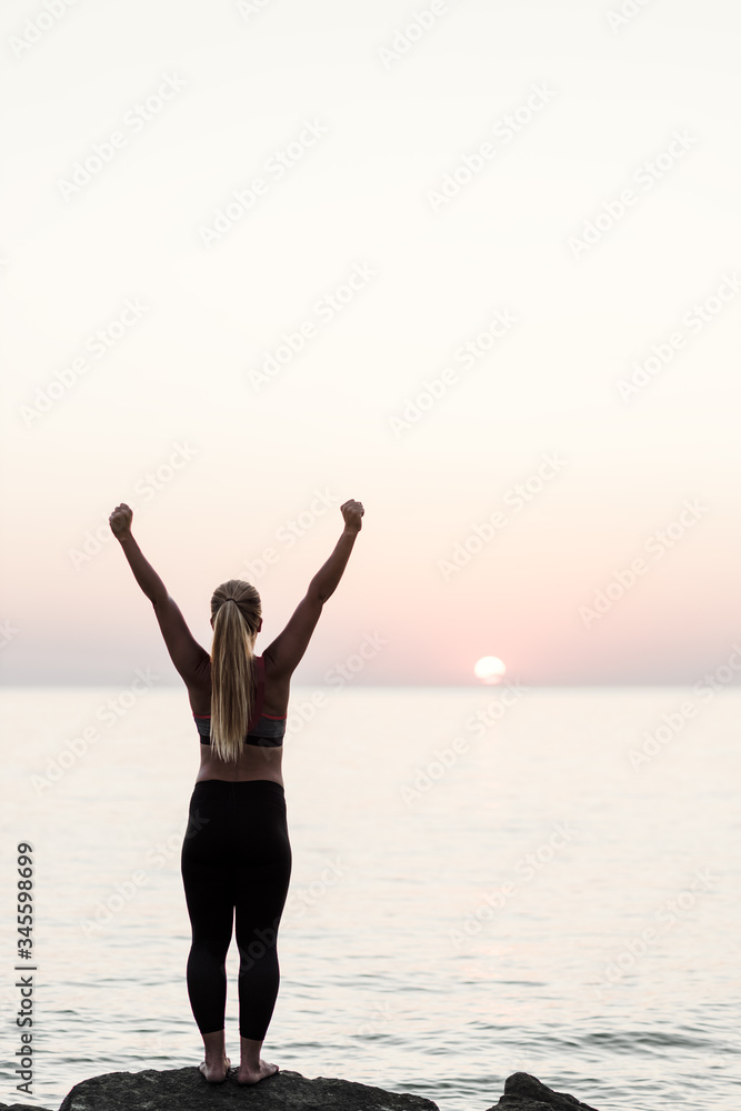 Young woman standing by the sea with arms raised in triumph