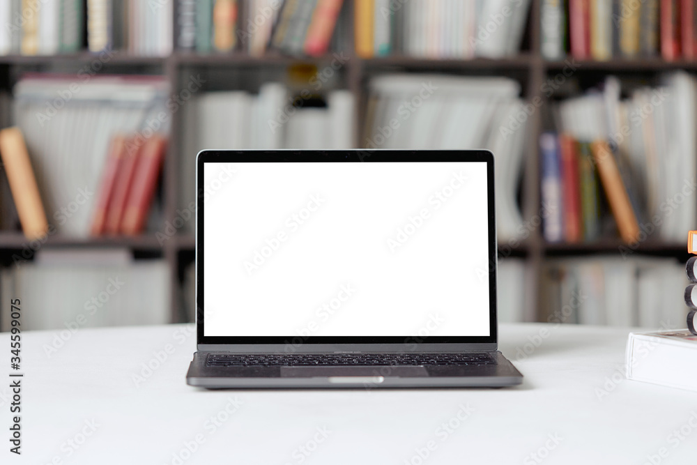 A laptop with copy space for text stands on a table in the library against the background of a bookshelf. A laptop with copy space for text stands on a table in the library against the background of a bookshelf.