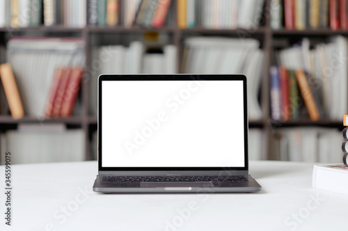A laptop with copy space for text stands on a table in the library against the background of a bookshelf.