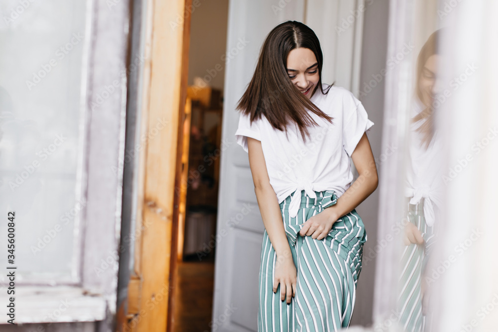 Fascinating european lady laughing while fooling around at home. Indoor portrait of carefree brunette girl in green pants enjoying weekend. Fascinating european lady laughing while fooling around at home. Indoor portrait of carefree brunette girl in green pants enjoying weekend.