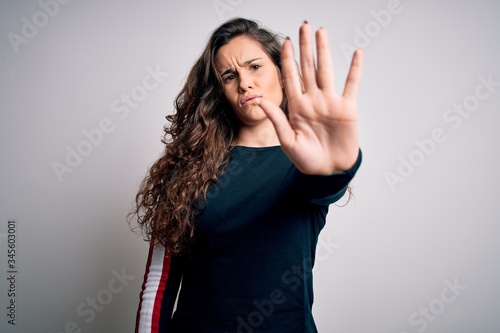 Young beautiful woman with curly hair wearing casual sweater over isolated white background doing stop sing with palm of the hand. Warning expression with negative and serious gesture on the face.