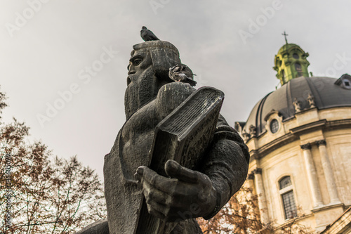 Monument of Ivan Fyodorov and dominican holy eucharist church in Lviv, Ukraine. Statue with bird on head and neo-baroque temple with cupola.  photo