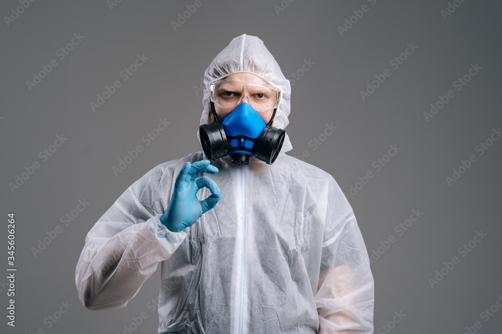 Doctor in protective medical suit, goggles and respirator is showing OK gesture, looking at the camera. Concept of Coronavirus COVID-19 Pandemic. Studio shot on dark background. Doctor in protective medical suit, goggles and respirator is showing OK gesture, looking at the camera. Concept of Coronavirus COVID-19 Pandemic. Studio shot on dark background.