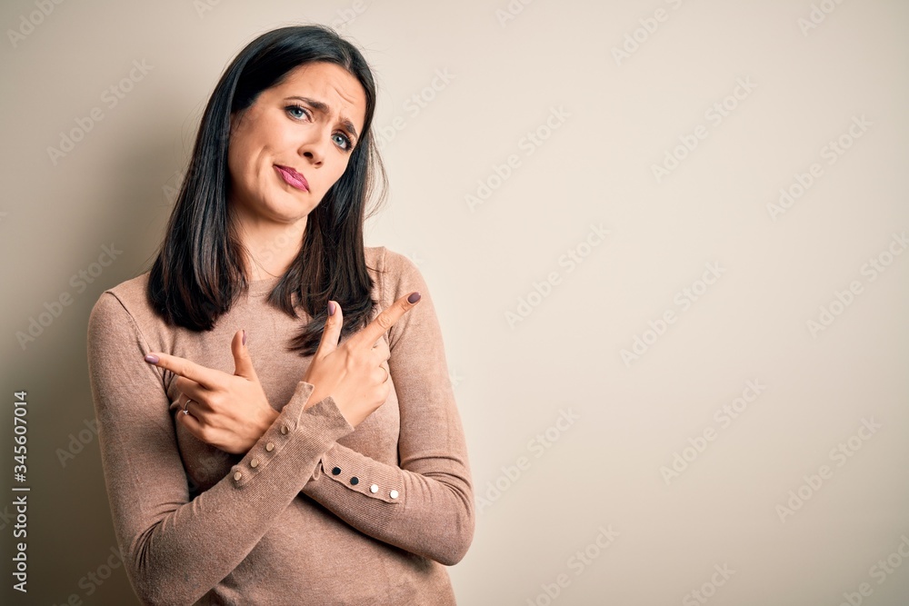 Young brunette woman with blue eyes wearing casual sweater over isolated white background Pointing to both sides with fingers, different direction disagree Young brunette woman with blue eyes wearing casual sweater over isolated white background Pointing to both sides with fingers, different direction disagree
