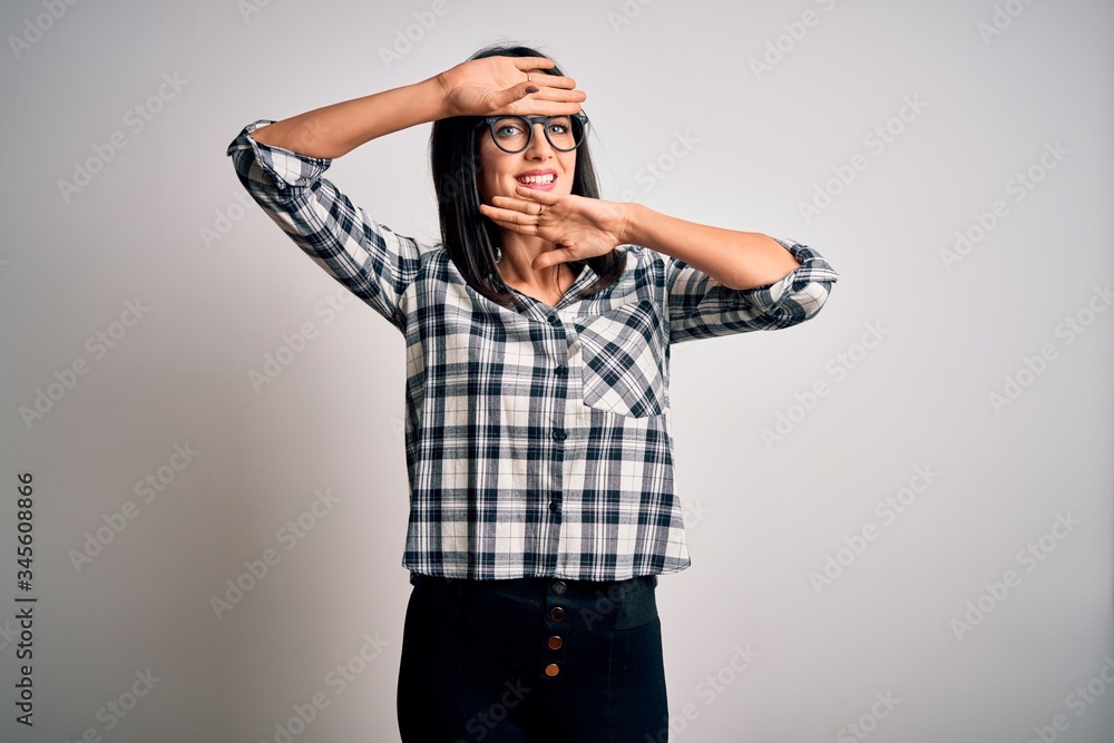 Young brunette woman with blue eyes wearing casual shirt and glasses over white background Smiling cheerful playing peek a boo with hands showing face. Surprised and exited