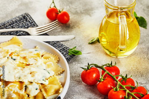 Tasty cooked ravioli with cream sauce, cherry tomatoes, sunflower oil and basil on a light wooden background.
