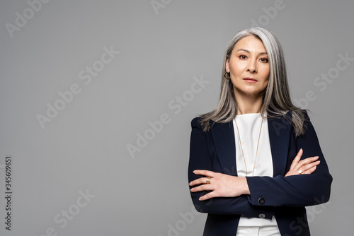 confident asian businesswoman with grey hair and crossed arms isolated on grey
