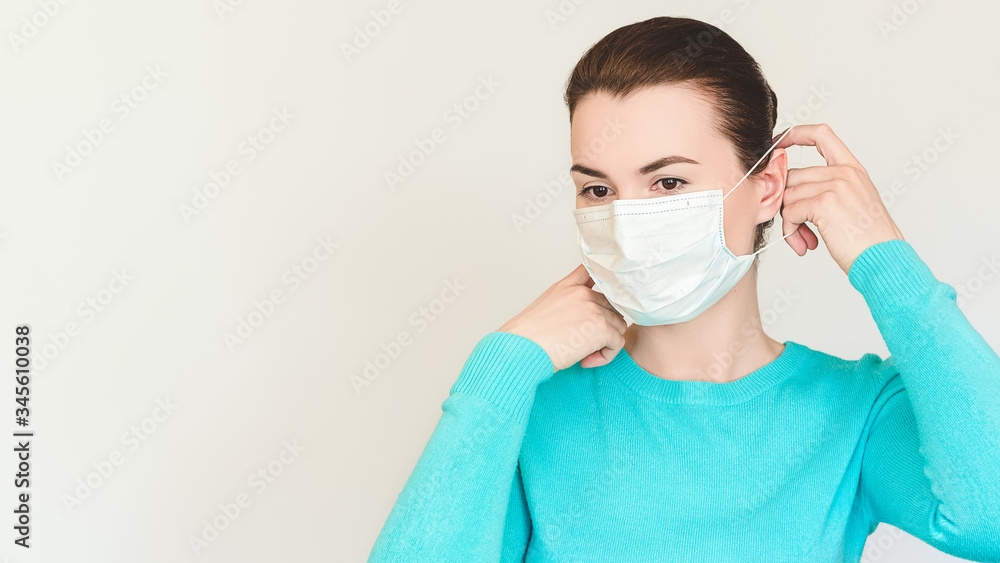 brunette woman in a blue sweater puts on a medical mask on a white background. Copy space for text. Virus protection concept