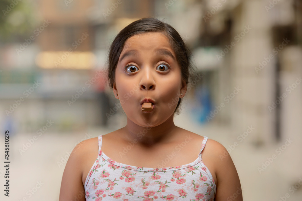 Portrait of a girl with a piece of chocolate in her mouth with eyes wide open and raised eyebrows
Portrait of a girl with a piece of chocolate in her mouth with eyes wide open and raised eyebrows