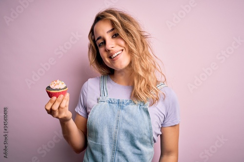 Young beautiful blonde woman eatimg chocolate cupcake over isolated pink background with a happy face standing and smiling with a confident smile showing teeth photo