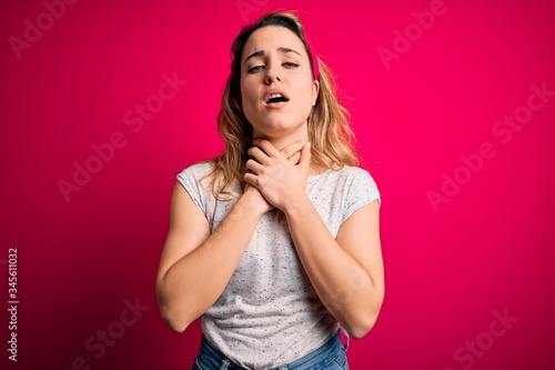 Young beautiful blonde woman wearing casual t-shirt standing over isolated pink background shouting and suffocate because painful strangle. Health problem. Asphyxiate and suicide concept.