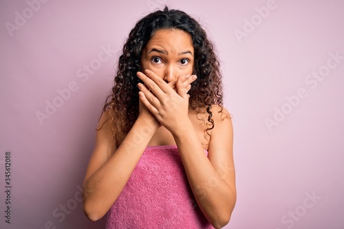 Young beautiful woman with curly hair wearing shower towel after bath over pink background shocked covering mouth with hands for mistake. Secret concept.