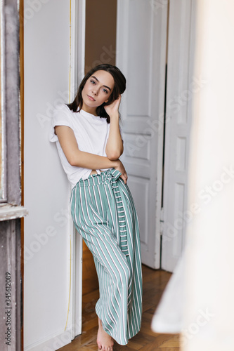 Full-length portrait of romantic brunette girl in pajamas chilling at home. Indoor shot of charming woman relaxing during rest in her apartment.