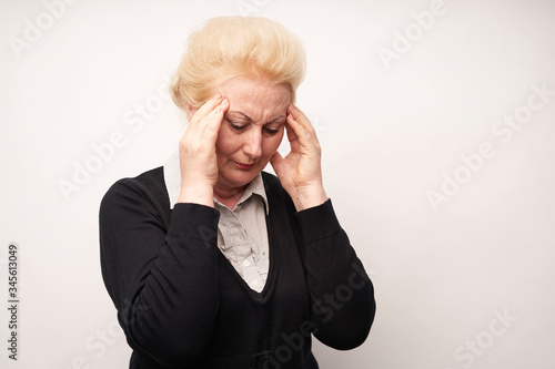 An elderly woman holds her hands on her sore head on a white background