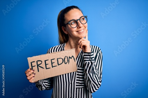 Young beautiful blonde woman with blue eyes holding banner with freedom message serious face thinking about question, very confused idea