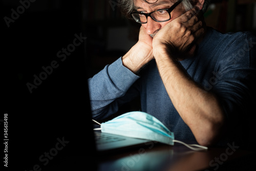 middle-aged man looking on computer at the news about global pandemic from corona virus and he worries, emotional distress, insomnia, concern for business and health in time of covid19 photo