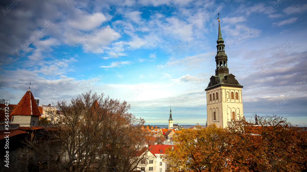 Autumn panorama of Tallinn from the fortress wall. View of the Church tower, autumn trees and the fortress wall. Blue textured sky with clouds