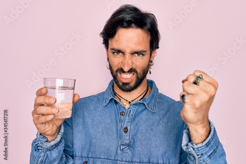 Young handsome hispanic bohemian hipster man with bear drinking a fresh glass of water annoyed and frustrated shouting with anger, crazy and yelling with raised hand, anger concept © Krakenimages.com