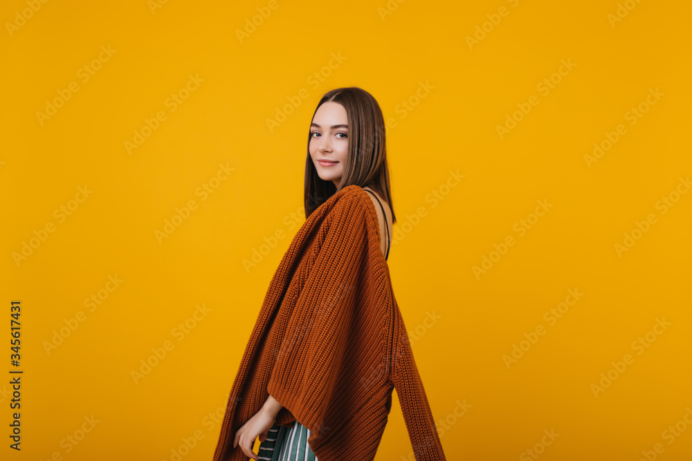 Naklejka premium Shy brunette girl posing in brown knitted sweater. Indoor portrait of interested european woman isolated on yellow background.
