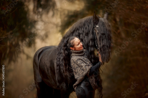 Woman with Black Beautiful Friesian stallion with long hair outdoor portrait in an autumn forest